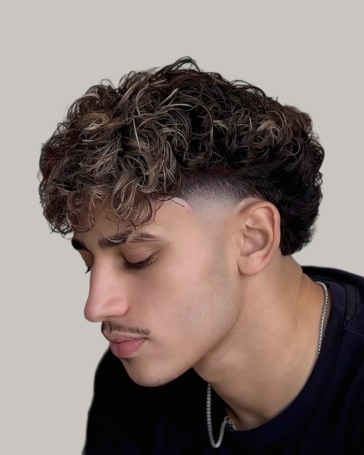 Young man with textured curls on top and a fade, seen from the side