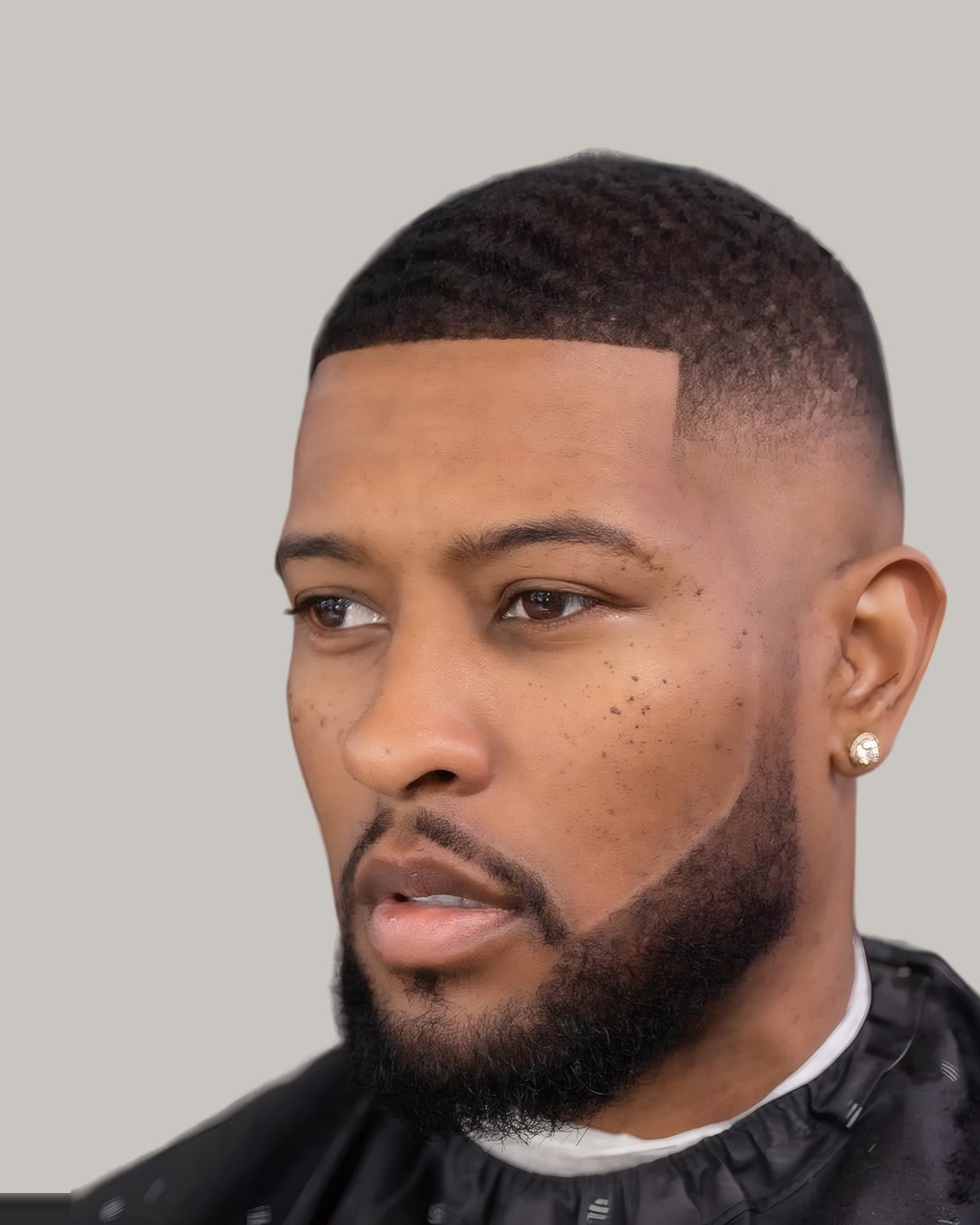 Bearded man with a short brushed-up top and a fade, seen from the side