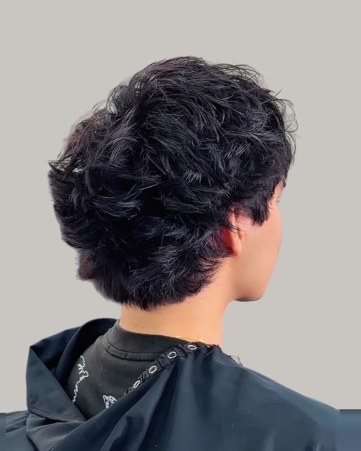 Man with dense dark curls and a drop taper, seen from behind at an angle