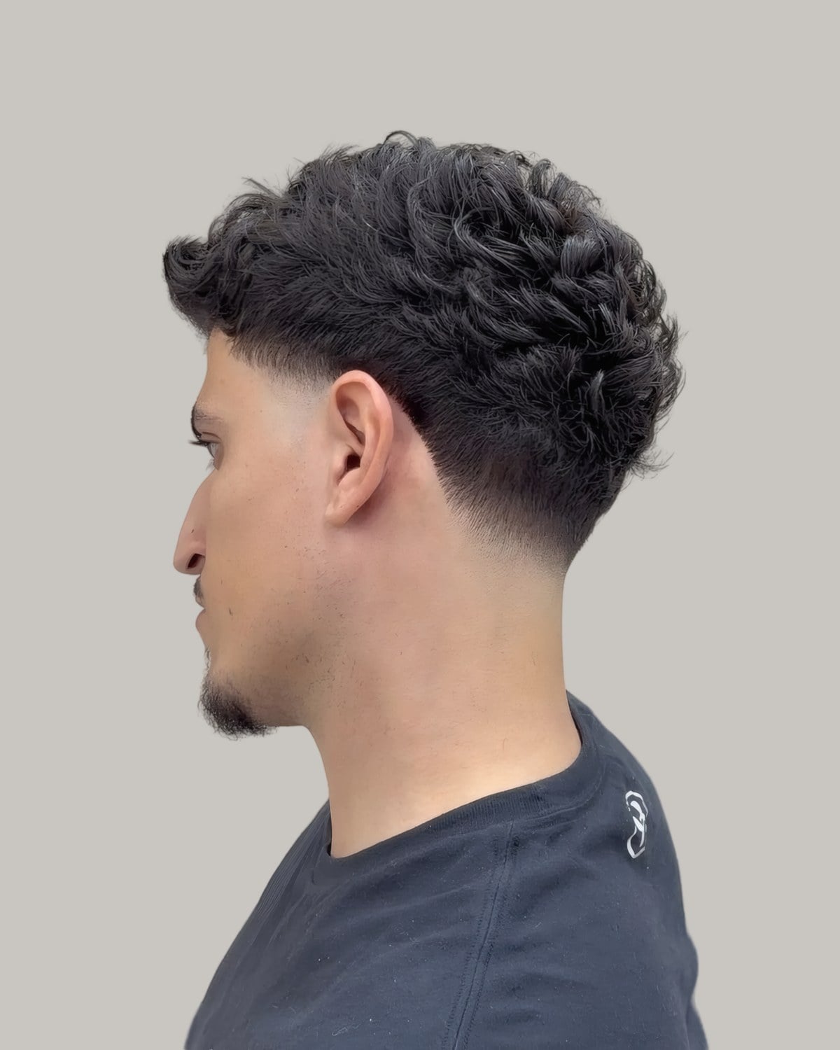 Man with a short curly top and a fade, seen in profile