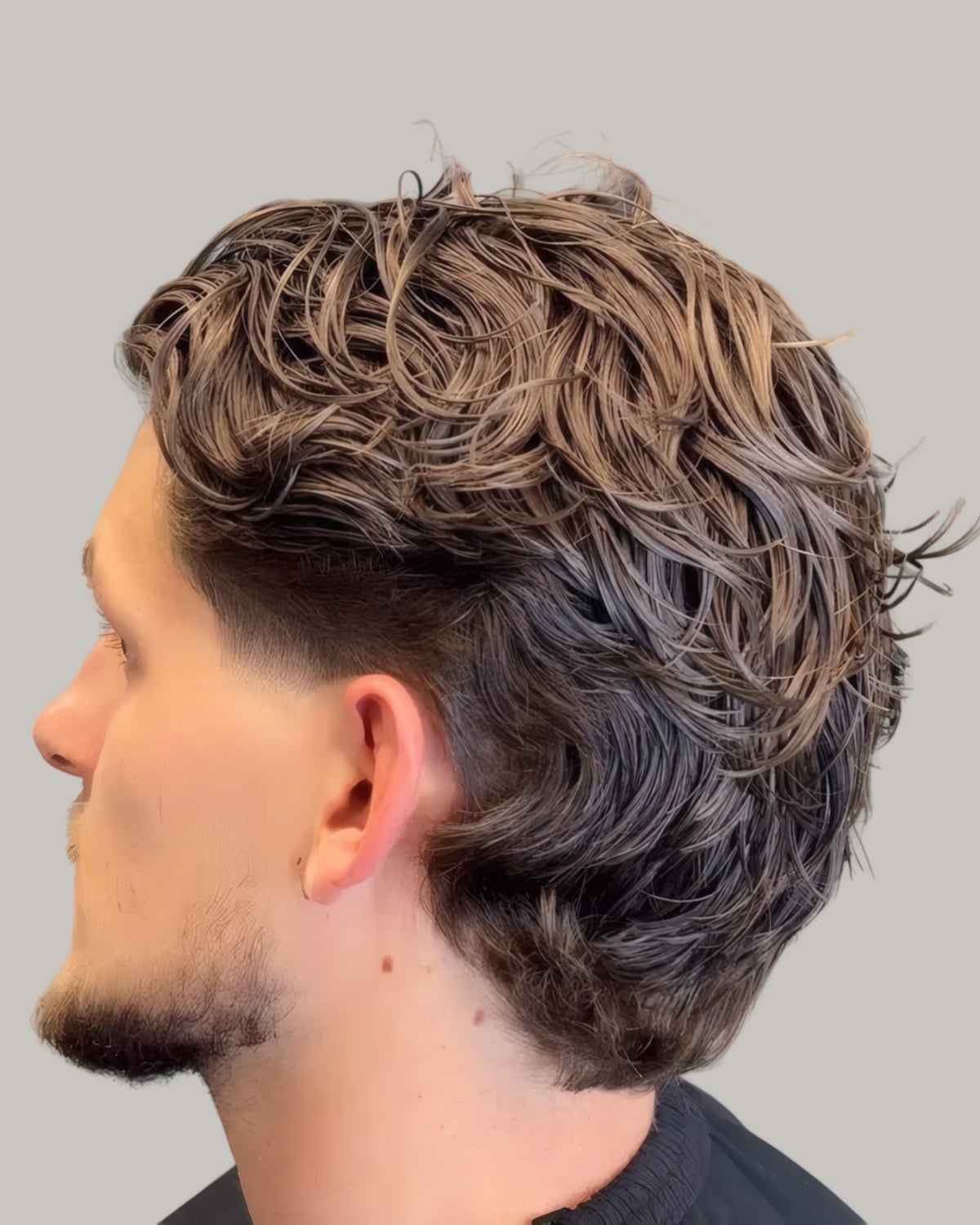 Man with long textured waves over a low fade, seen in profile