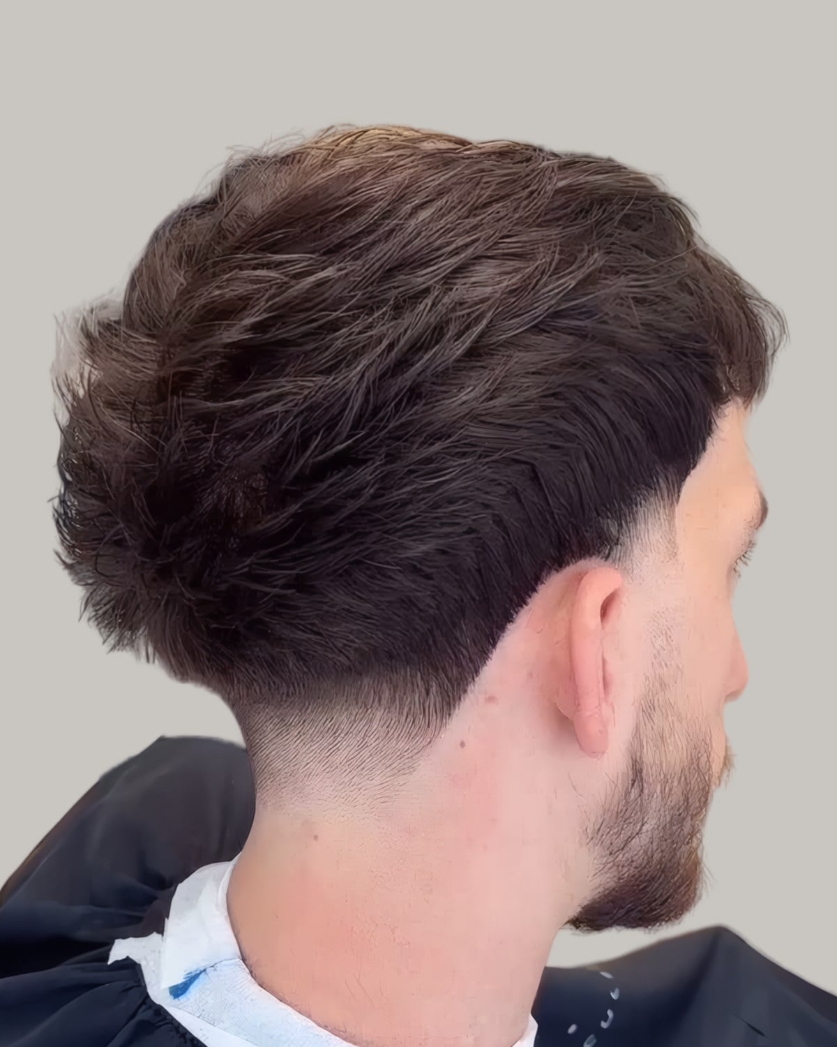 Man with a thick textured top and a skin fade, seen from behind at an angle
