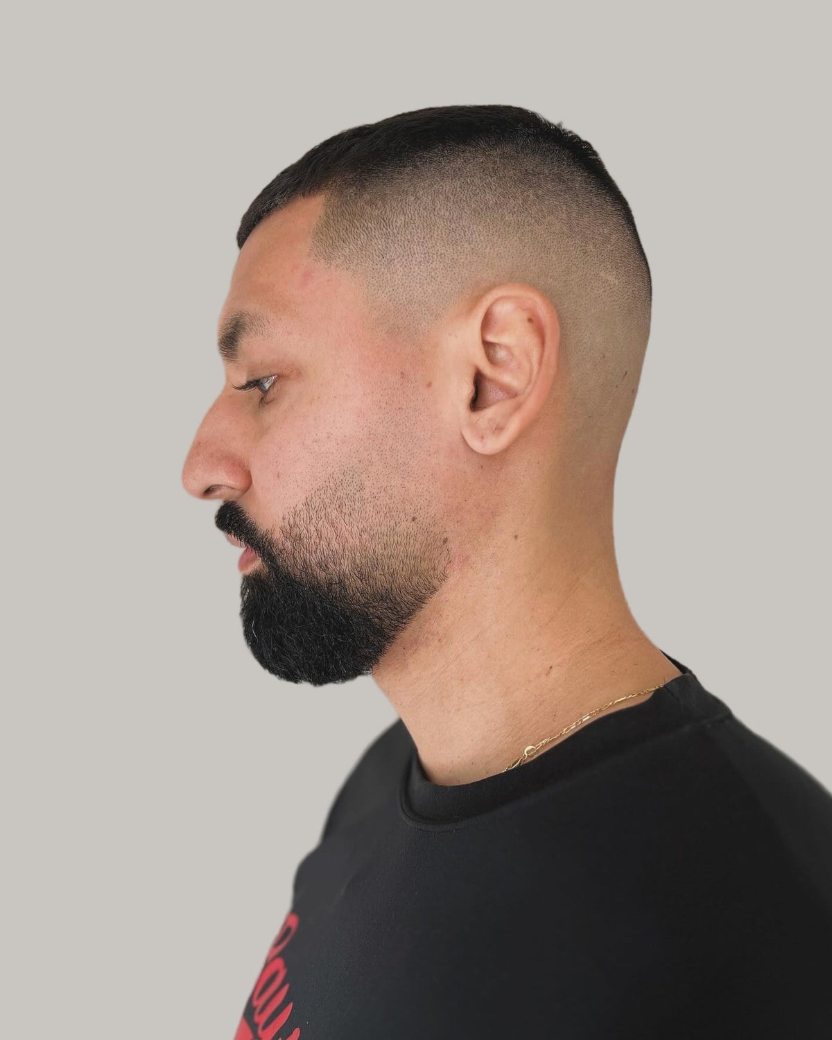 Man with a full dark beard and a high bald fade under a short top, seen in profile
