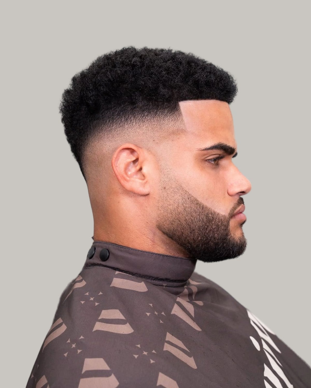 Bearded man with a squared-off afro top, a line-up and a high fade, seen in profile