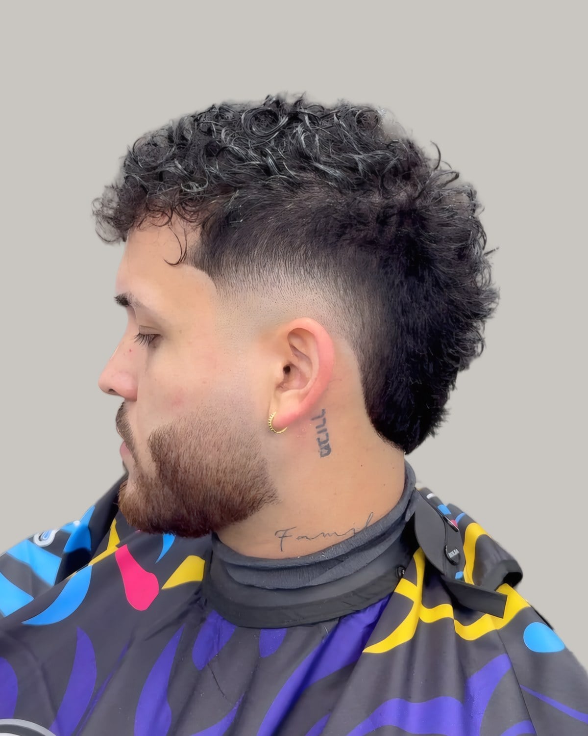 Bearded man with dark curls on top and a burst fade around the ear, seen at an angle