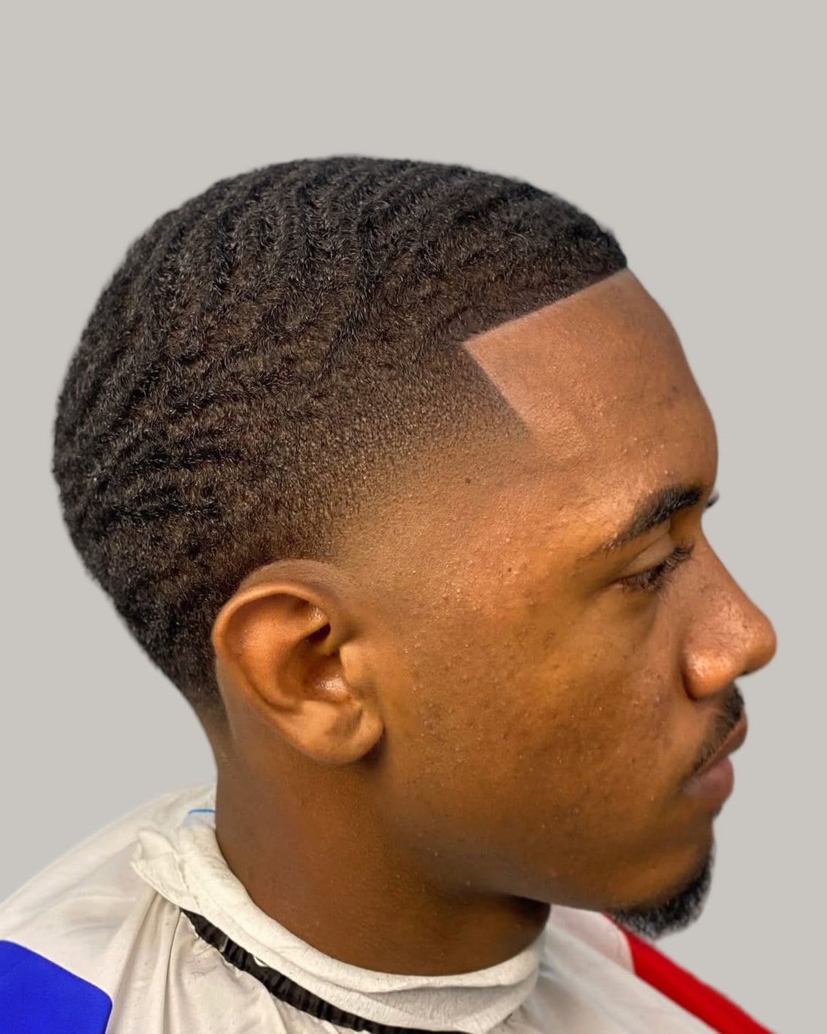 Man with short waves on top, a hard line-up and a low fade, seen in profile