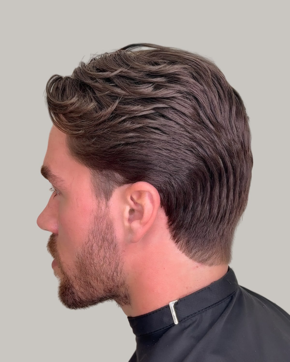 Man with stubble and long swept-back waves over tapered sides, seen in profile