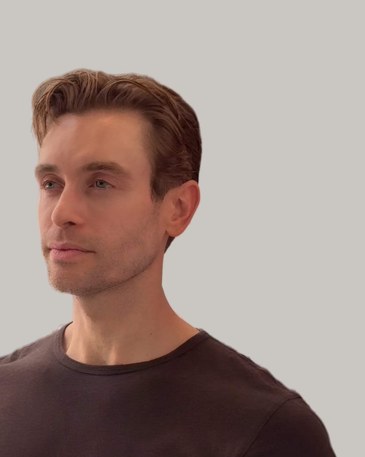 Man with stubble and a side-swept comb-over over tapered sides, seen at an angle