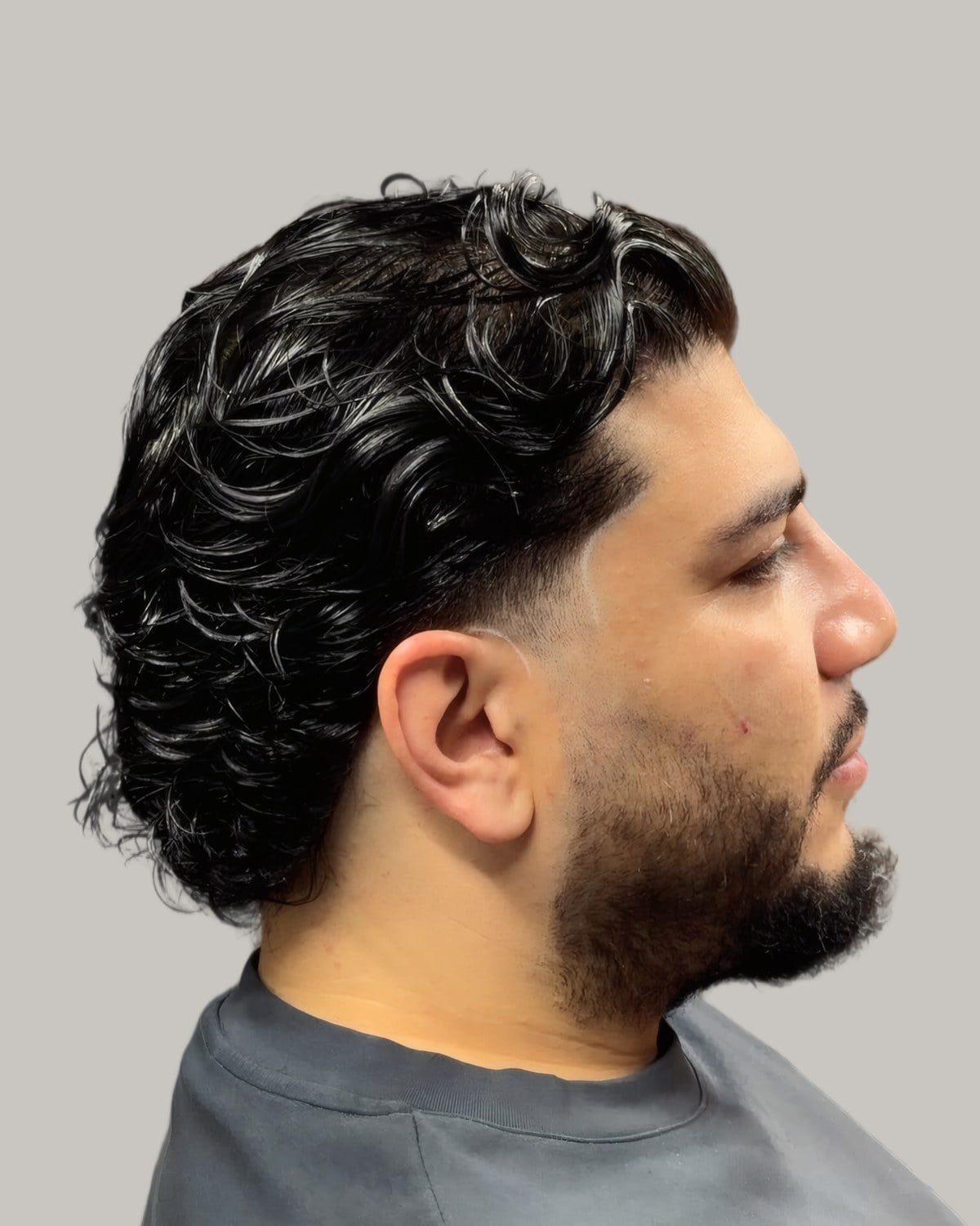 Bearded man with long loose curls on top and a low fade, seen at an angle