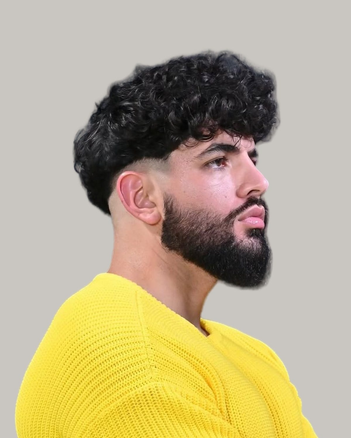 Bearded man in a yellow sweater with tight curls on top and a high fade, seen in profile