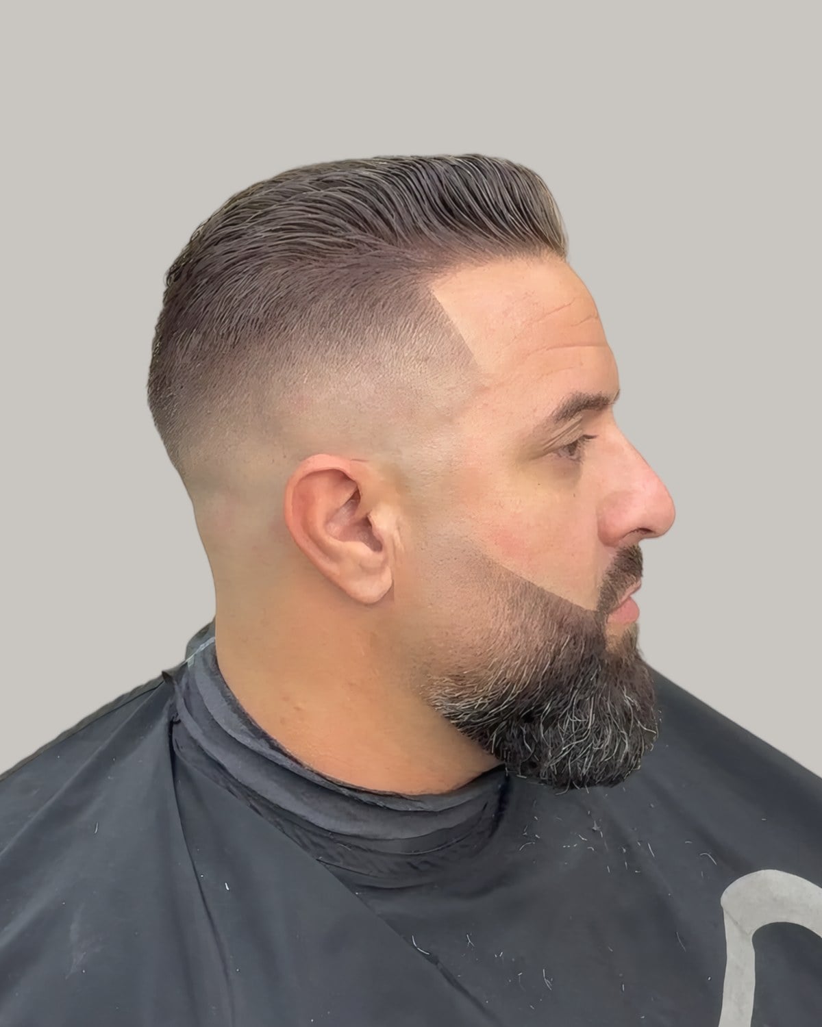 Bearded man with a slicked-back comb-over and high faded sides, seen at an angle