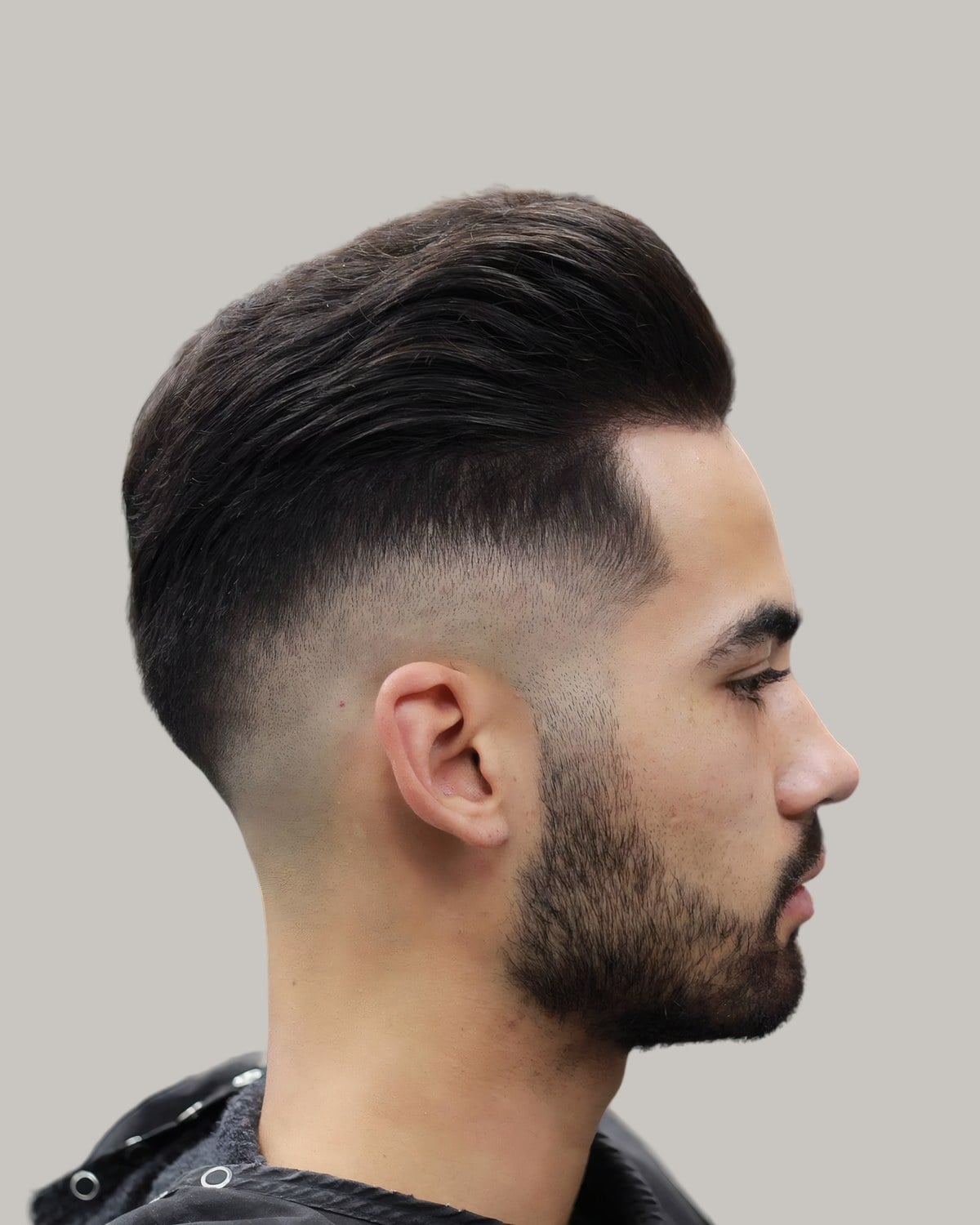 Bearded man with a long top blow-dried back and a high fade, seen in profile