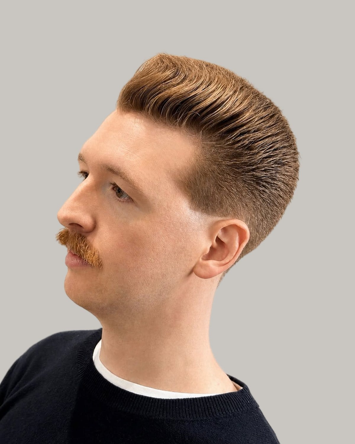 Man with a red moustache and a swept-up pompadour over faded sides, seen in profile