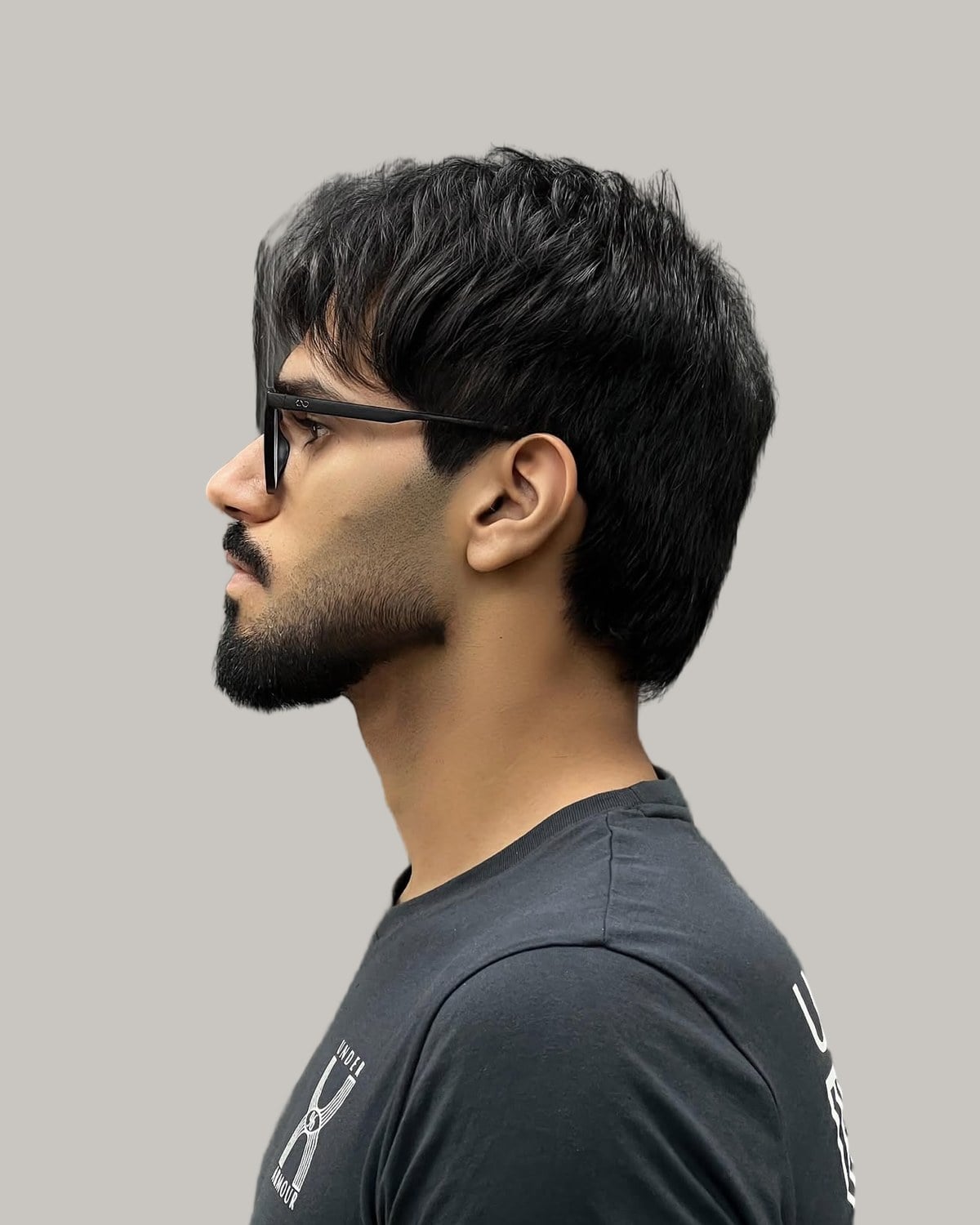 Bearded man in glasses with a messy textured top and a low taper, seen in profile