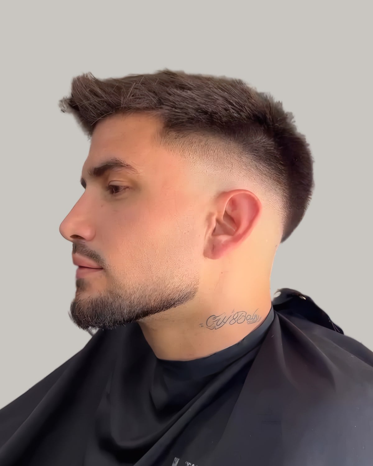 Bearded man with a short textured top pushed up at the centre and a mid fade, seen in profile