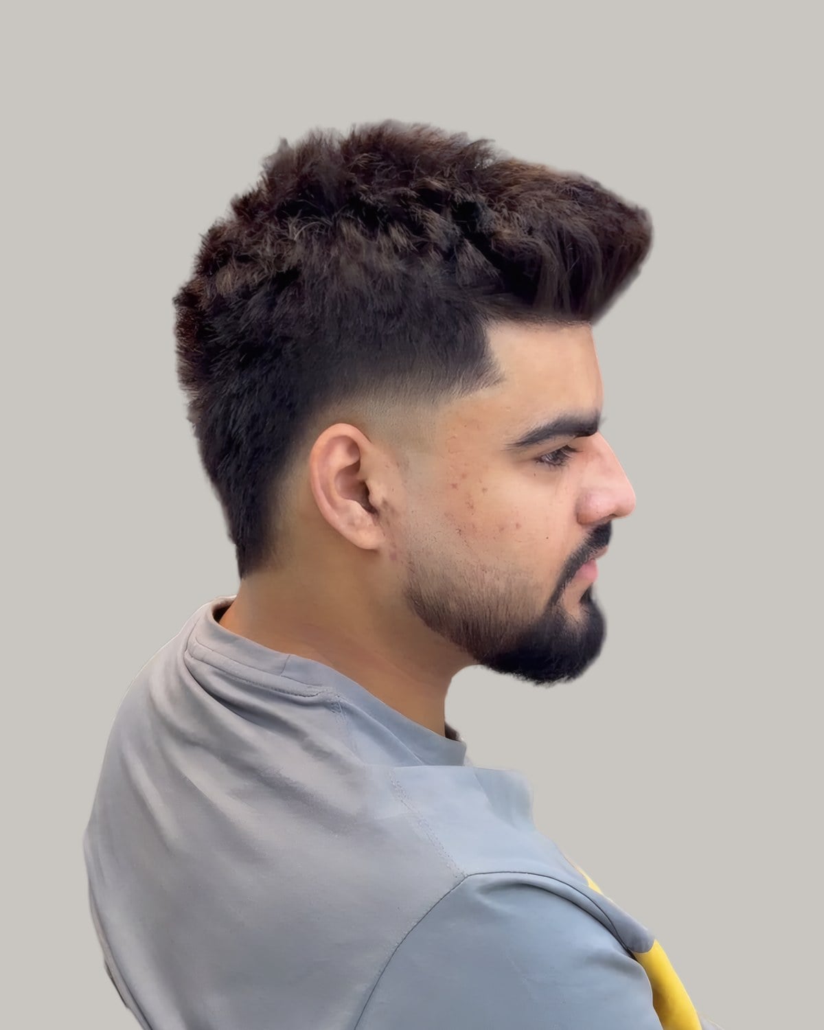 Bearded man with a textured top pushed up into a ridge and a mid fade, seen in profile