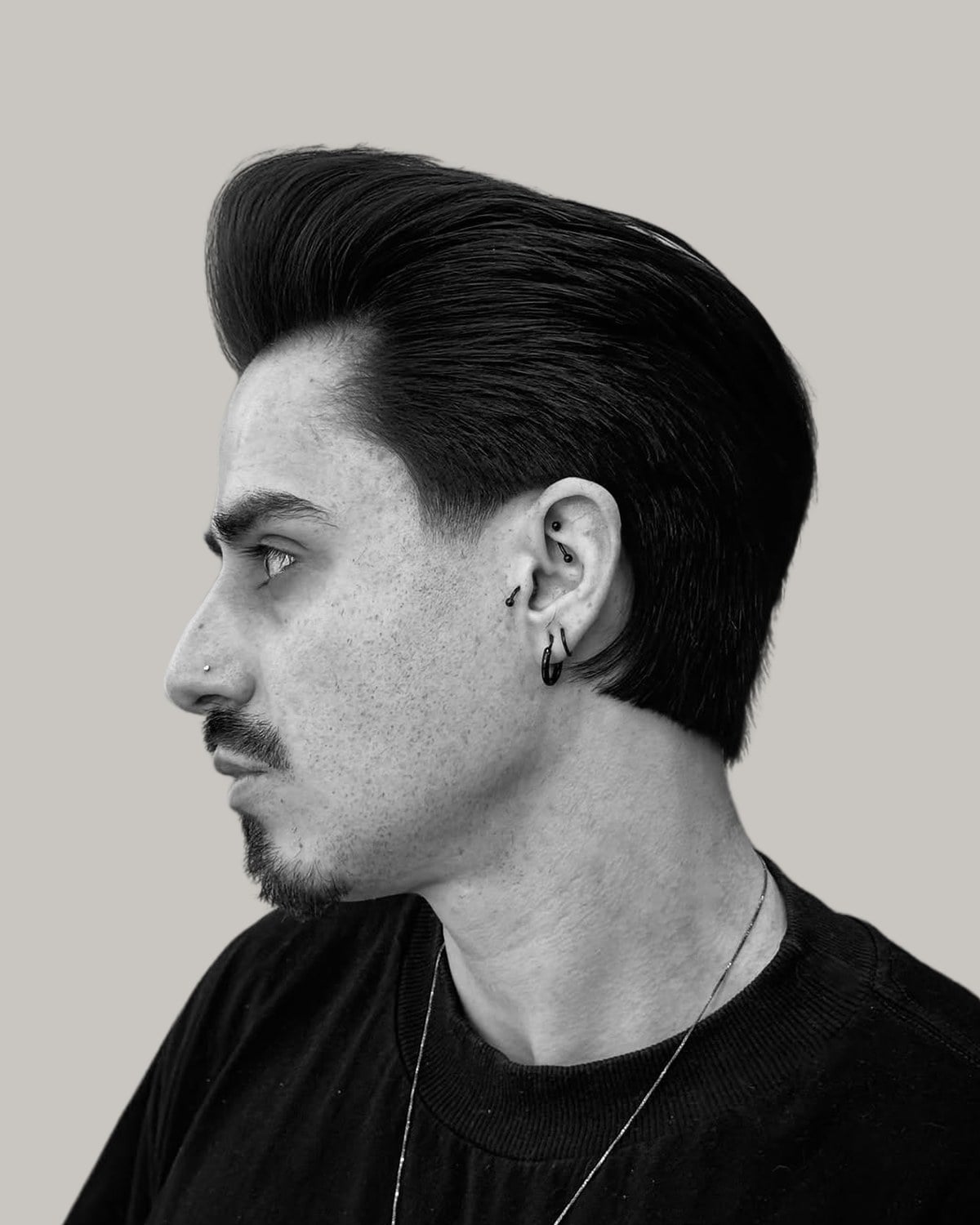 Man with a moustache and a tall slicked pompadour, in black and white, seen in profile