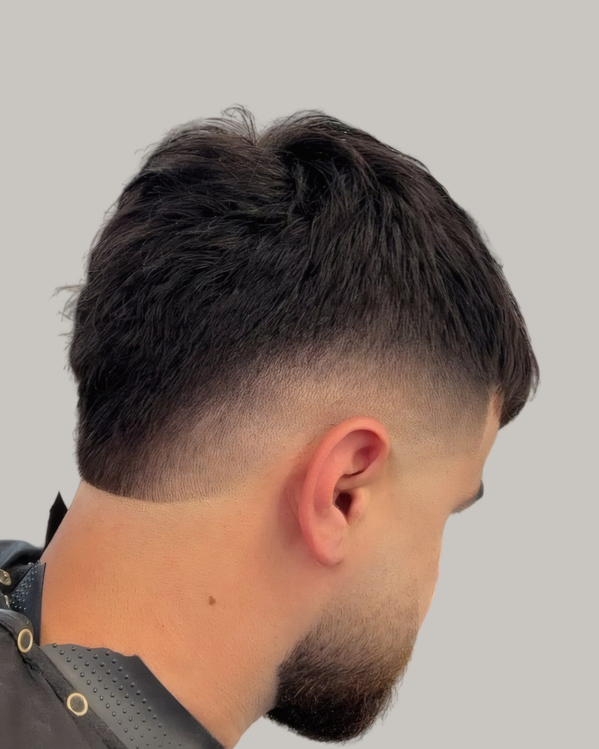 Bearded man with a thick dark top and a drop fade, seen from behind at an angle