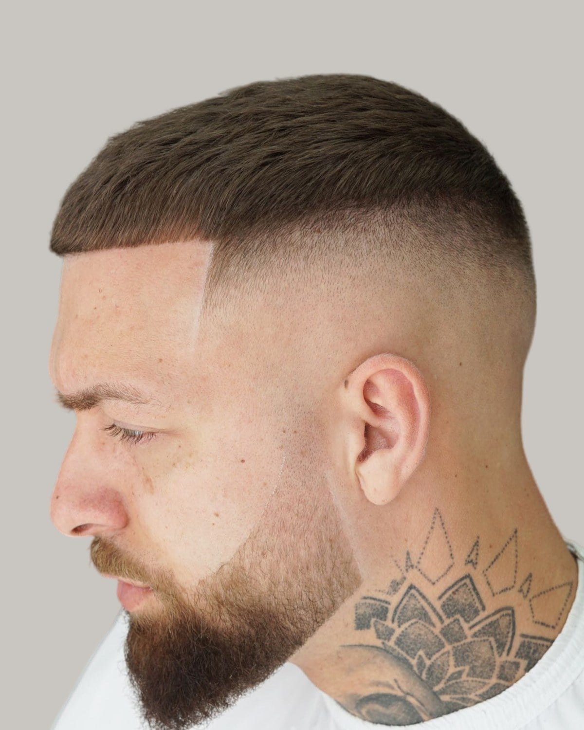 Bearded man with a short crop, a straight fringe and a skin fade, a mandala tattoo on his neck, seen in profile