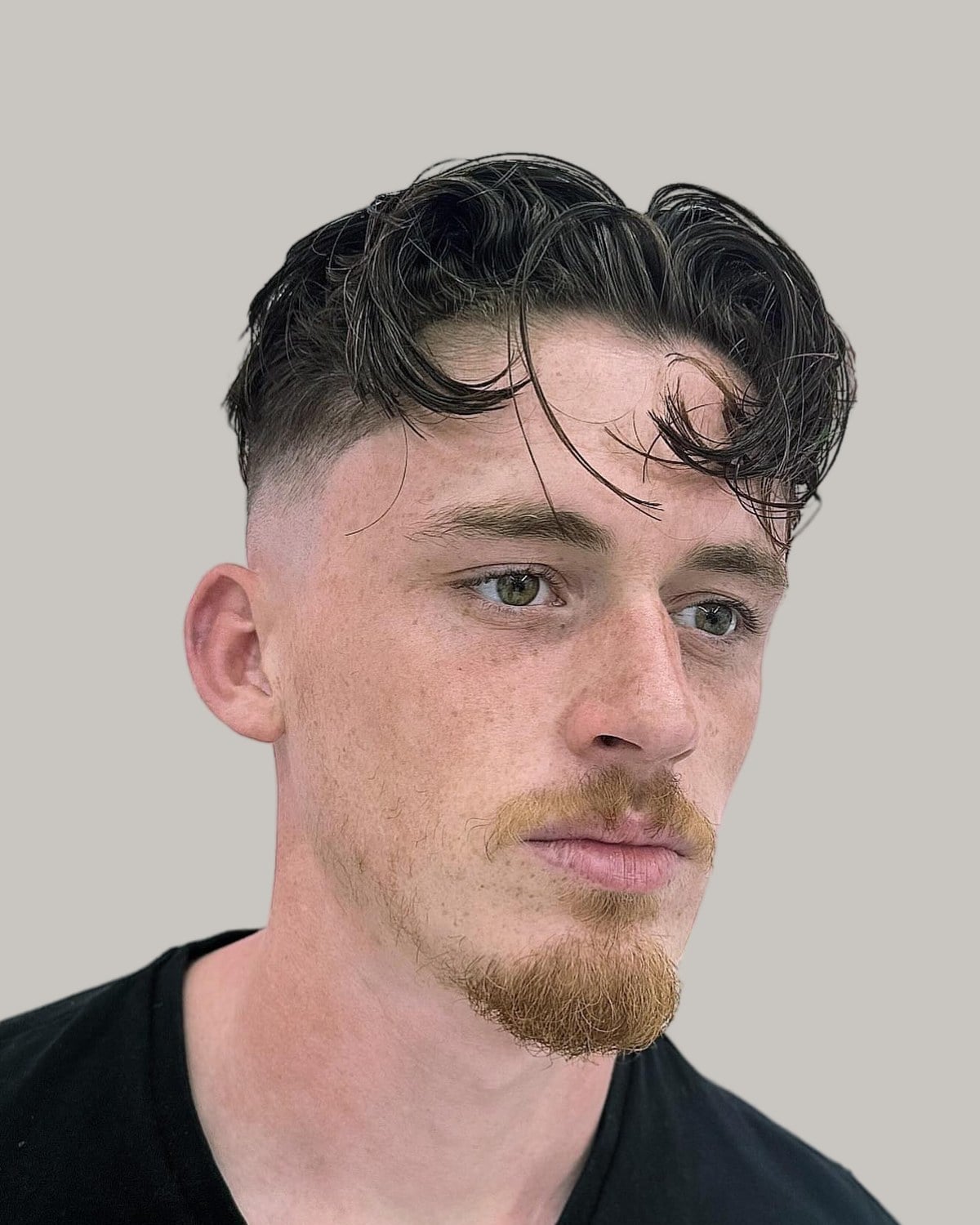Man with a ginger goatee and dark wavy hair parted in the middle over a high skin fade, seen at an angle