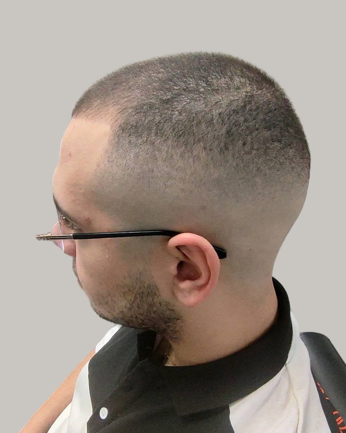 Man in glasses with a very short buzz and a low fade, seen from the side