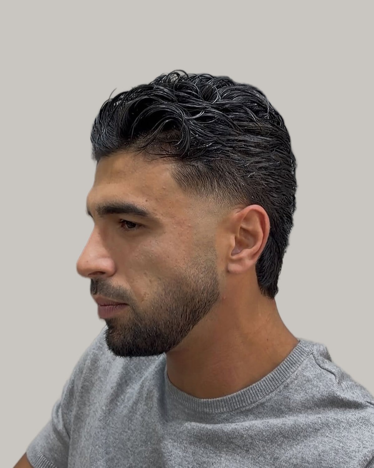 Bearded man with a wavy textured top and a fade that runs into the beard, seen at an angle