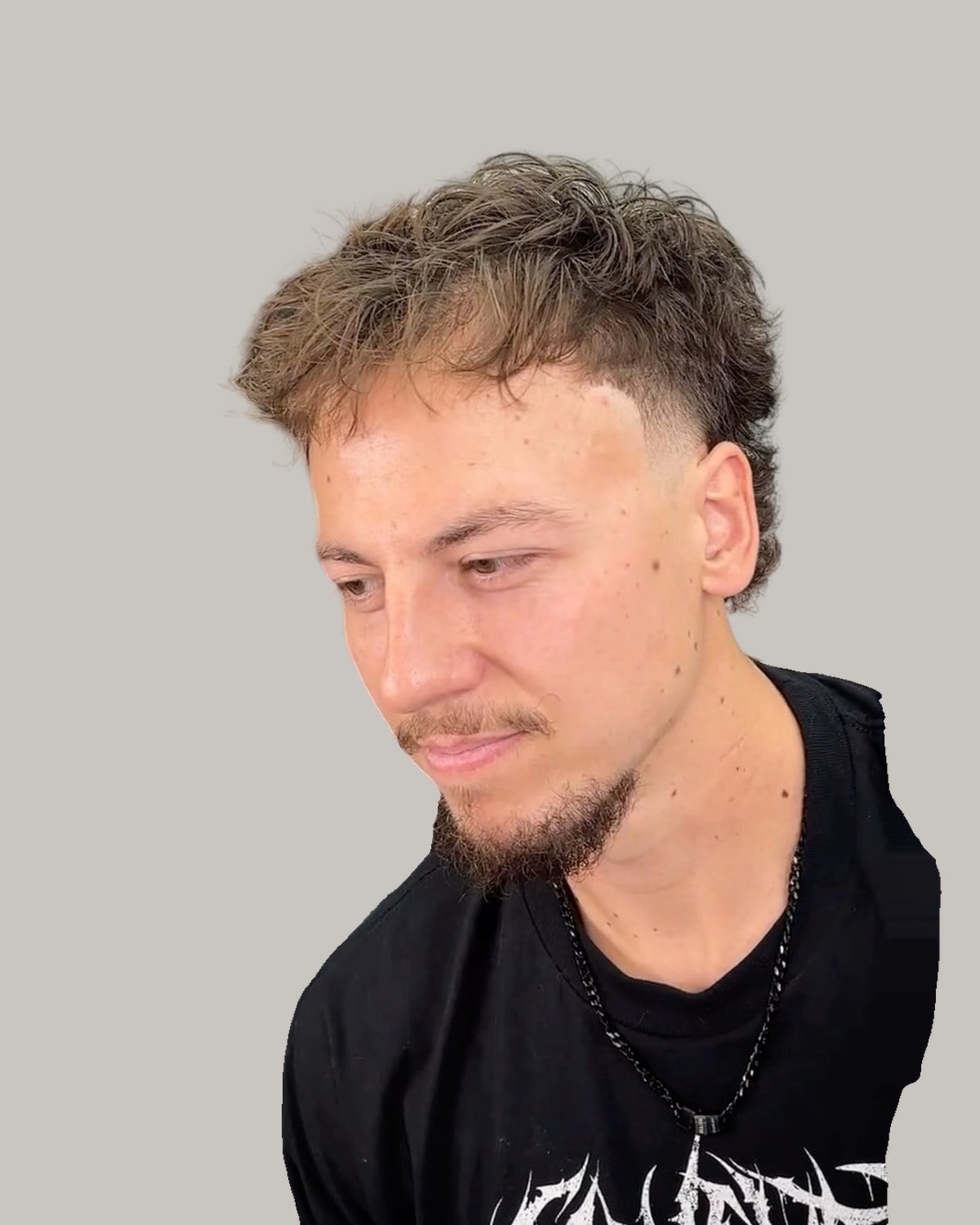Man with a curly fringe and a goatee, looking down to the side