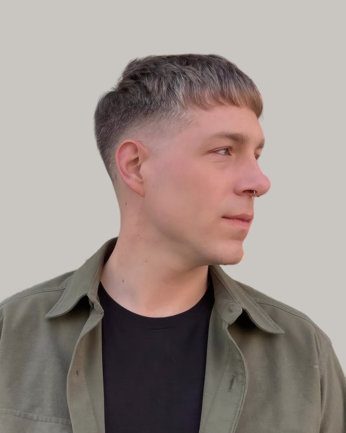Man with a French crop and a short fringe, in an olive jacket, looking to the side