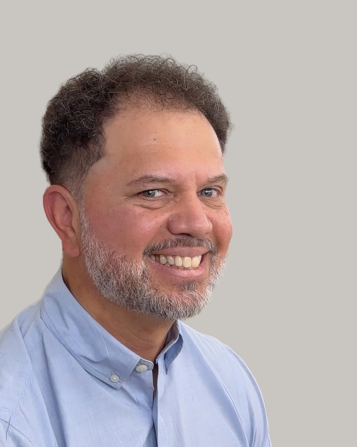 Smiling man with short curly dark hair, a high hairline and a grey beard