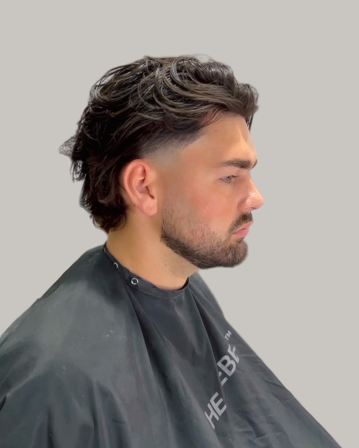 Bearded man with long hair swept back and a low fade, seen in profile