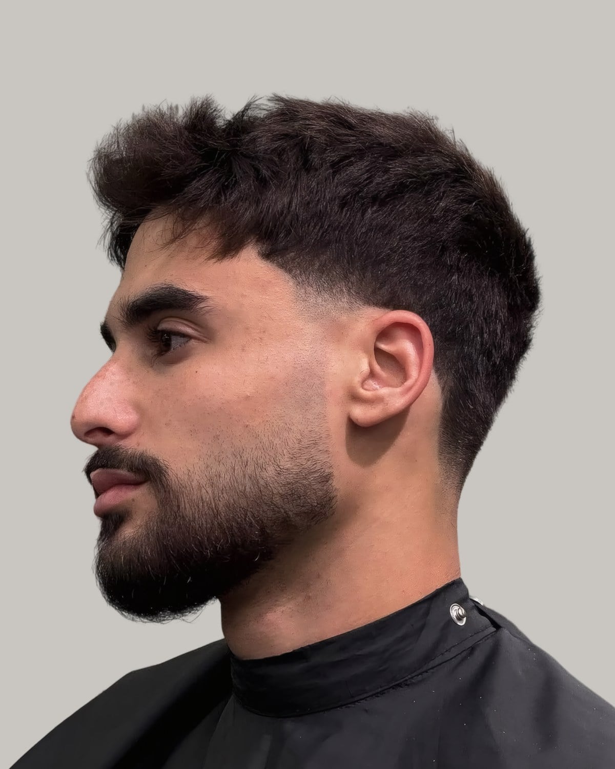 Bearded man with a textured top and a mid fade, seen in profile