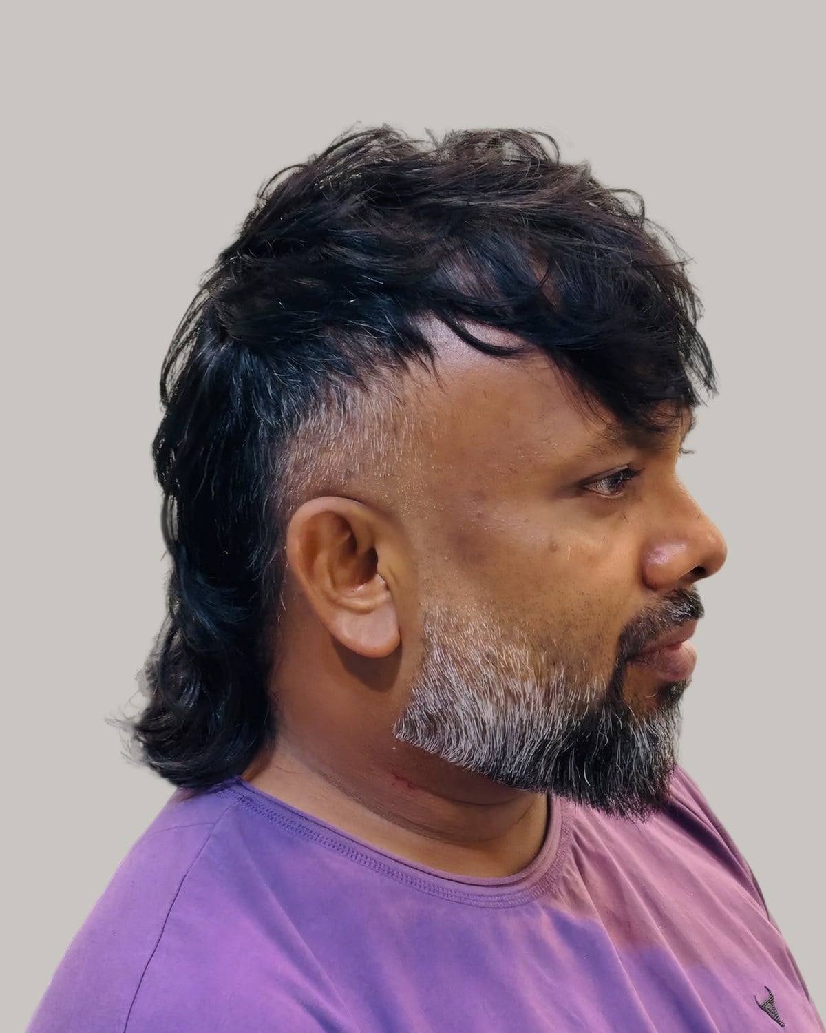 Man with a mullet, shaved sides and a grey beard, seen in profile