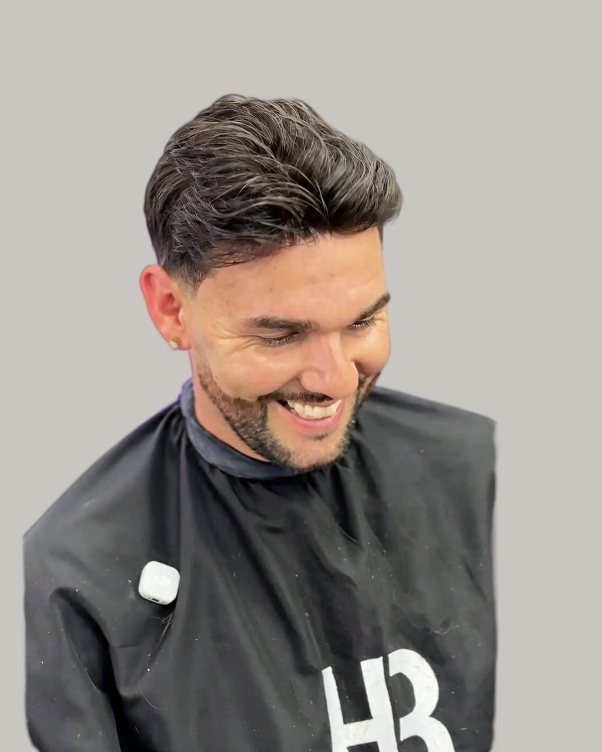 Smiling bearded man with a short quiff, in a barber's cape