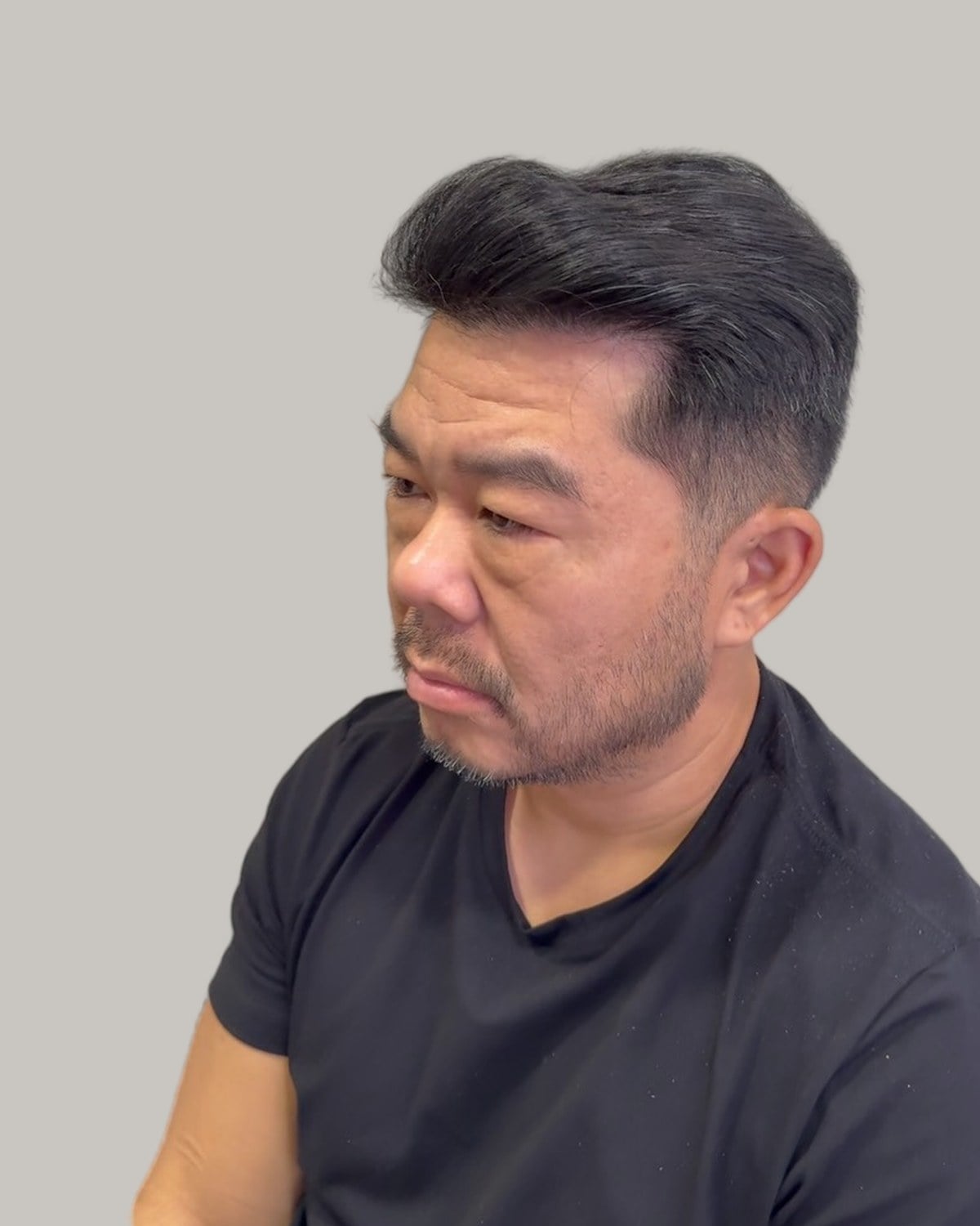 Man with a side-swept cut and a goatee, looking down to the side