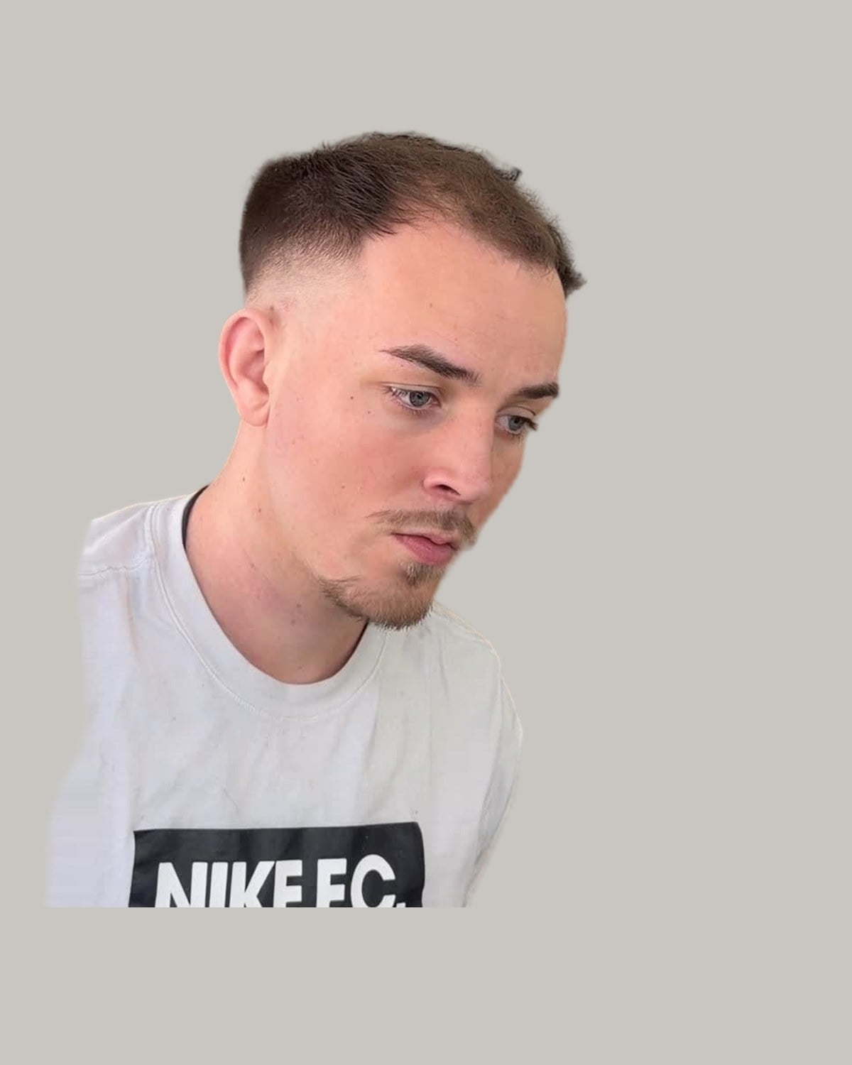 Man with a short crop, a mid skin fade and a receding hairline, looking down