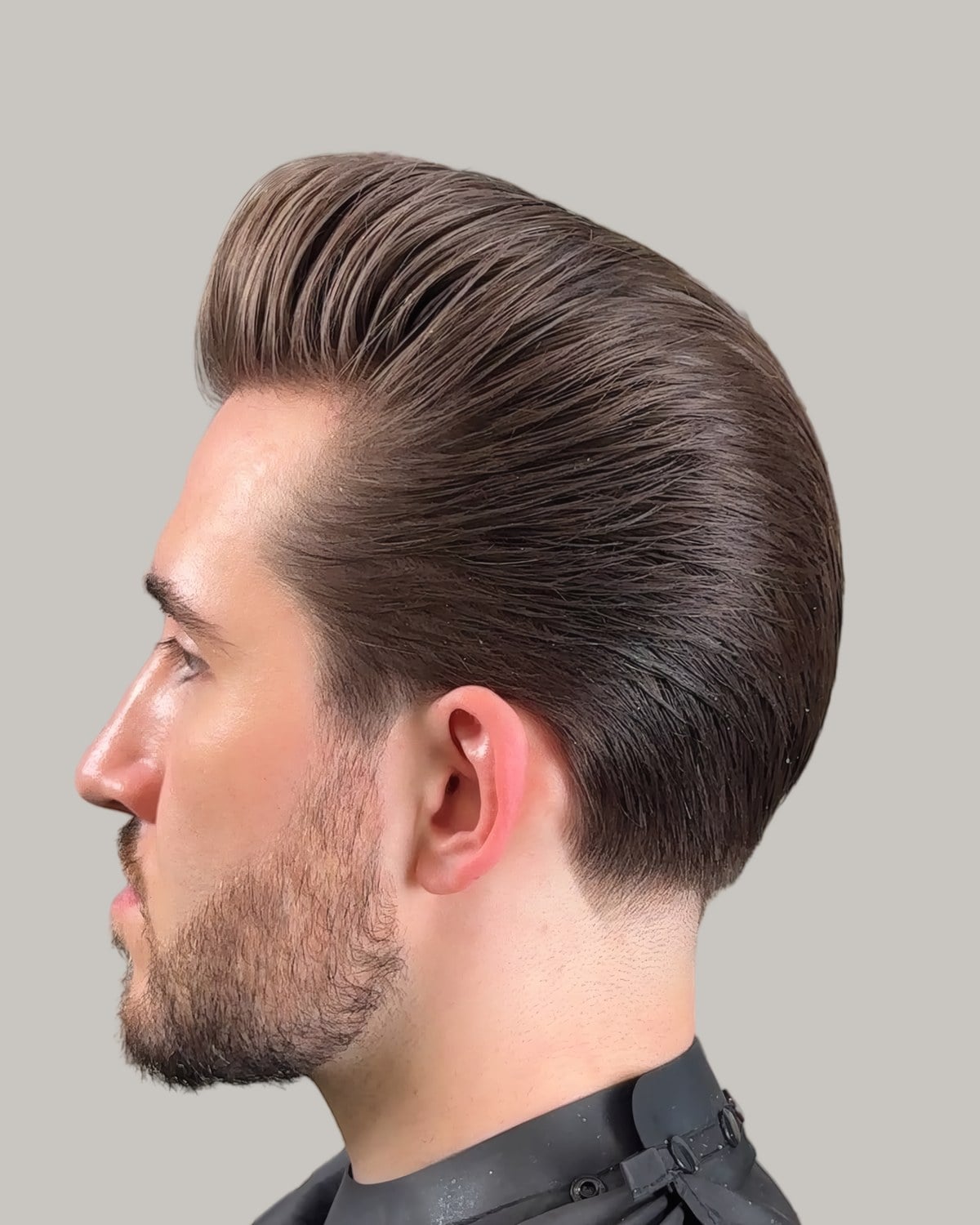 Man with a slick back pompadour and a beard, seen in profile