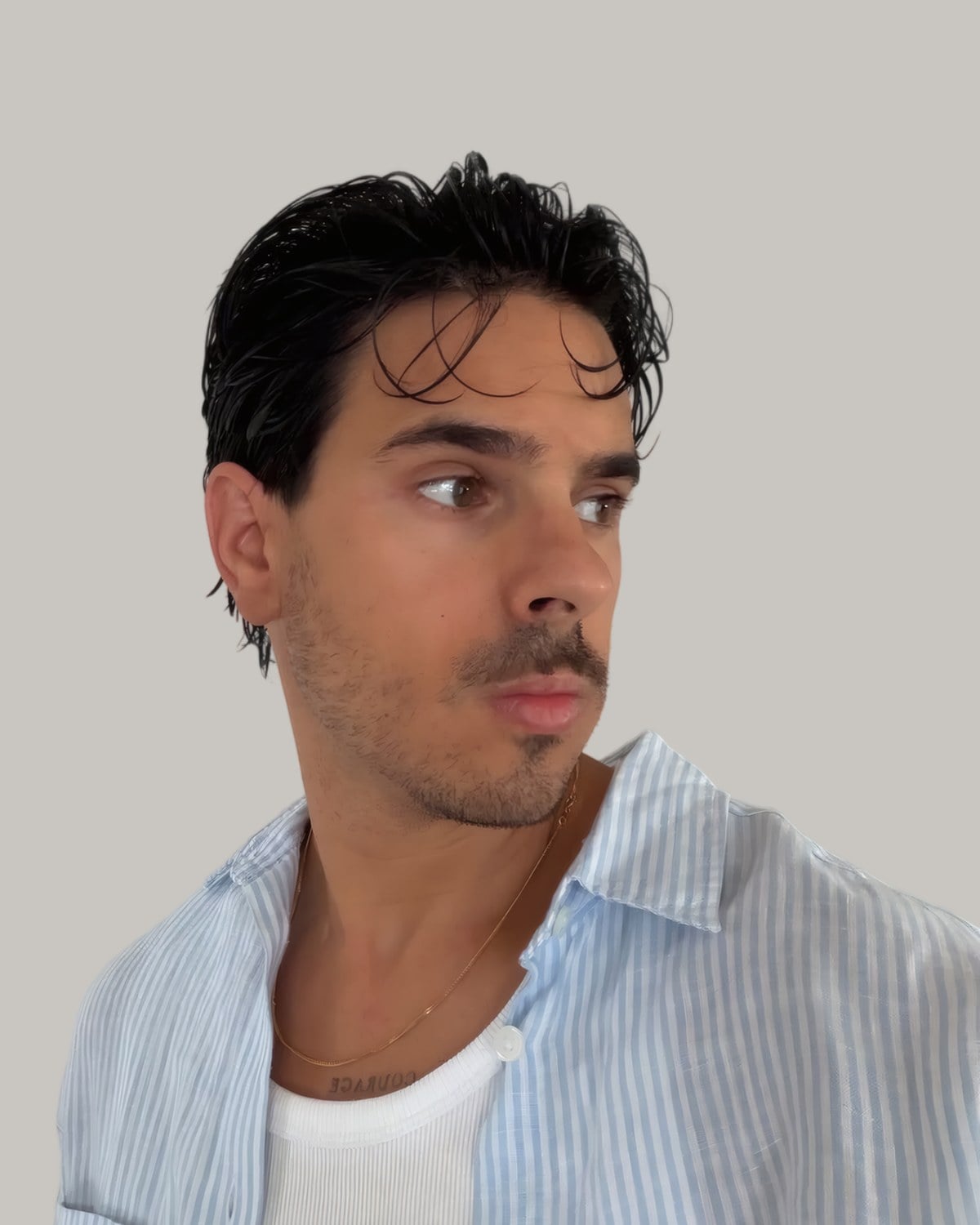 Man with medium-length wet-look hair swept back, in a striped shirt