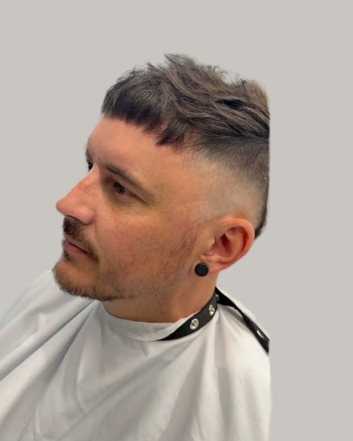 Man with a textured fringe and a fade, in a barber's cape, looking to the side