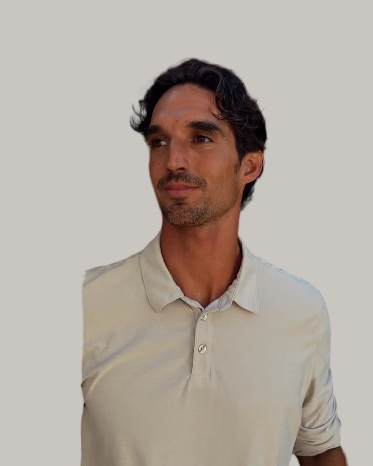 Man with wavy medium-length hair and stubble, in a polo shirt, looking to the side