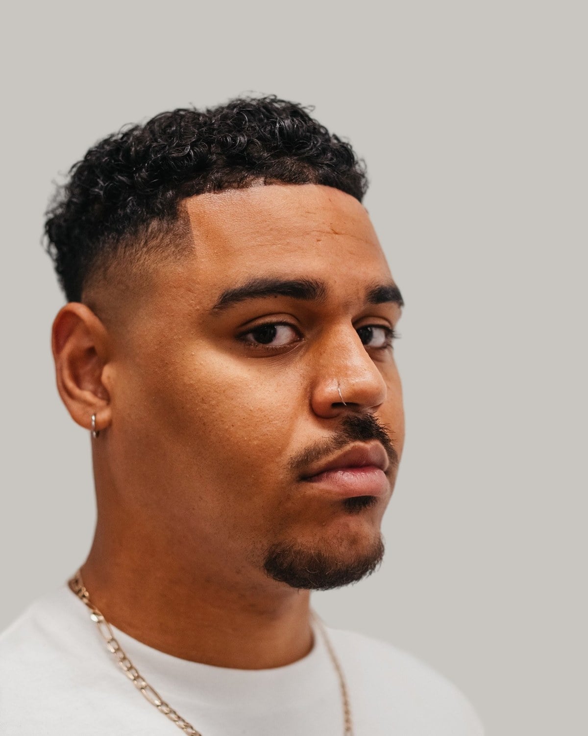 Man with a short curly top, a skin fade and a goatee, in a white T-shirt