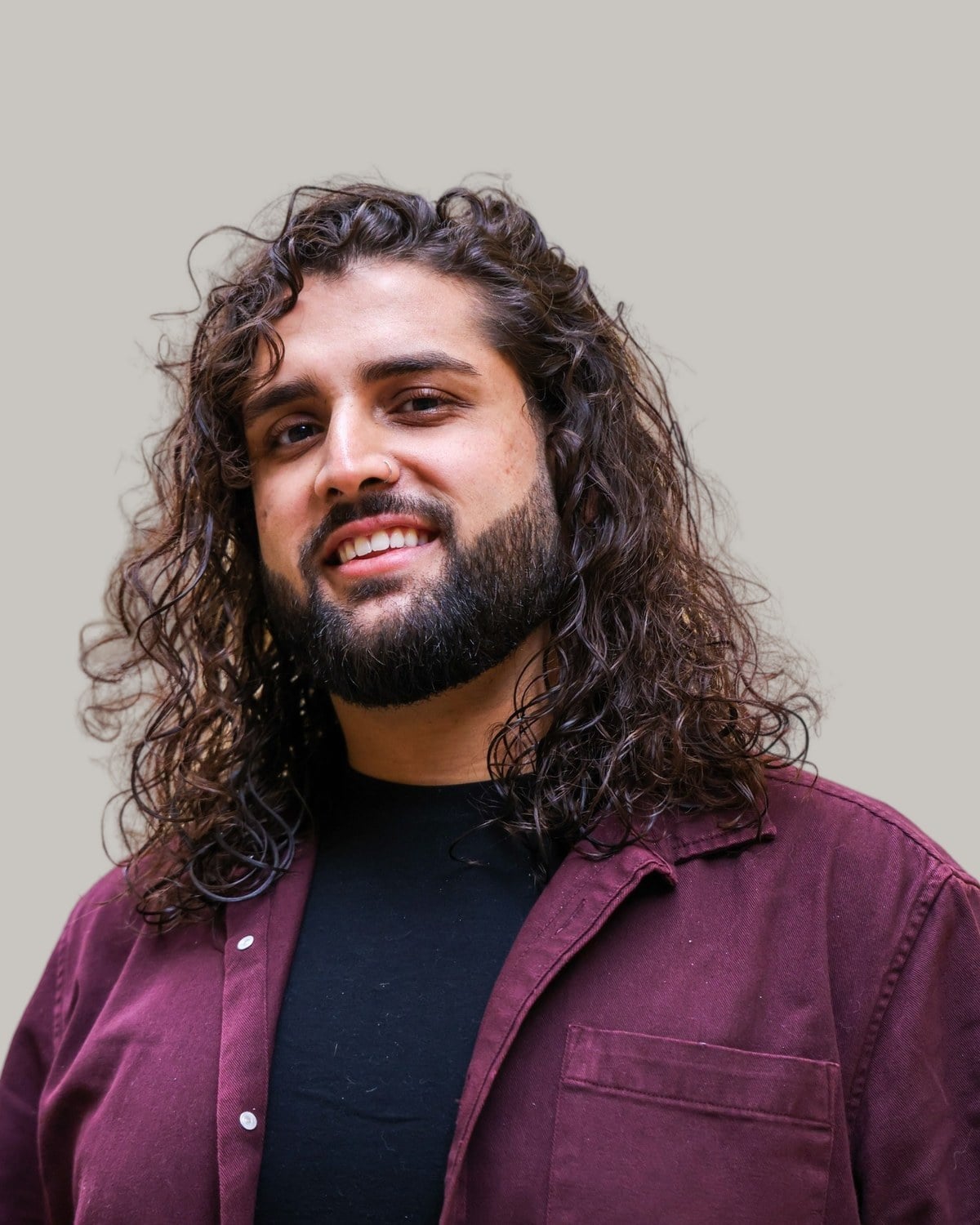 Smiling bearded man with long, dark curly waves past his shoulders, in a burgundy shirt