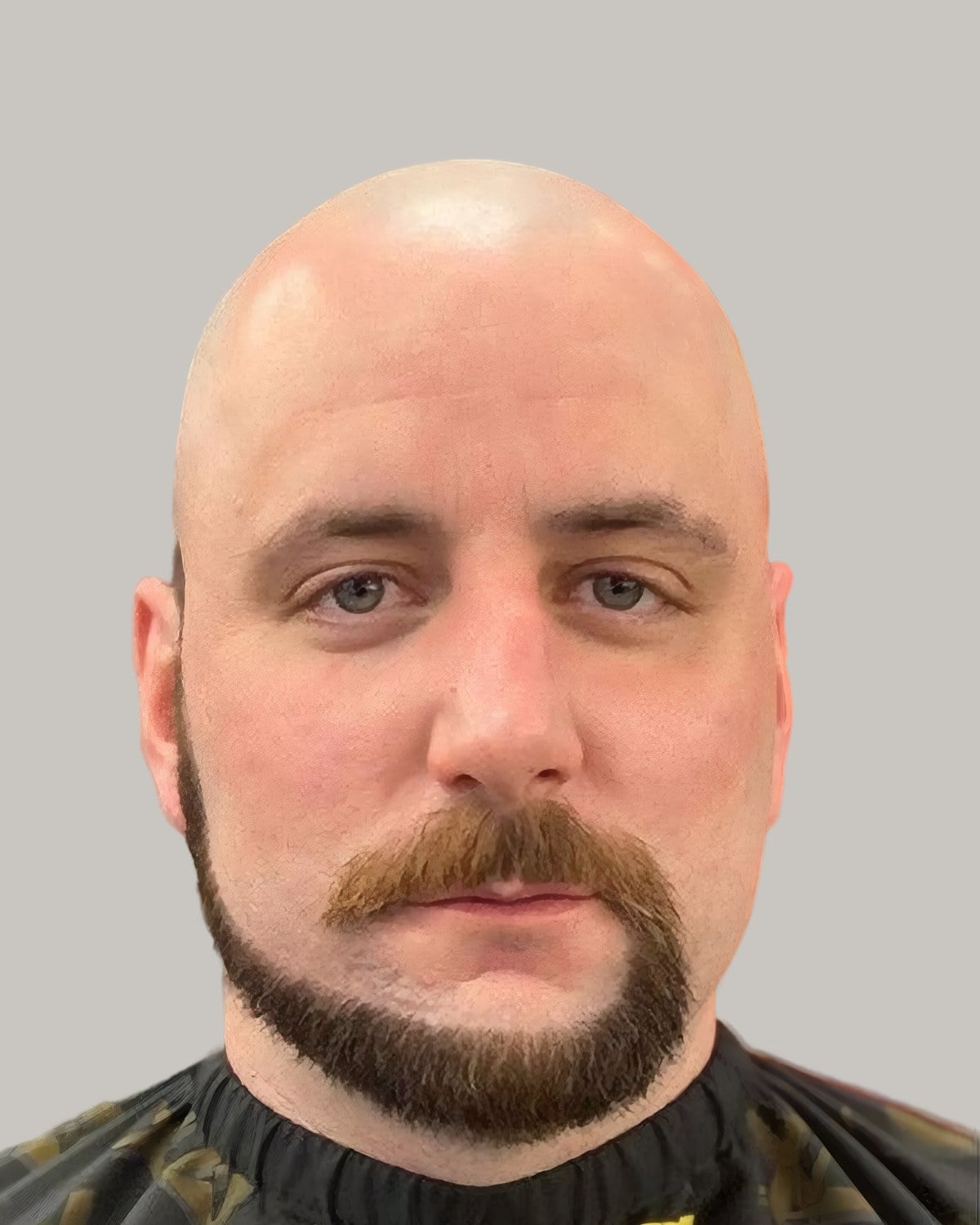 Man with a clean-shaven head, a horseshoe mustache and a narrow beard along the jaw, in a barber's cape