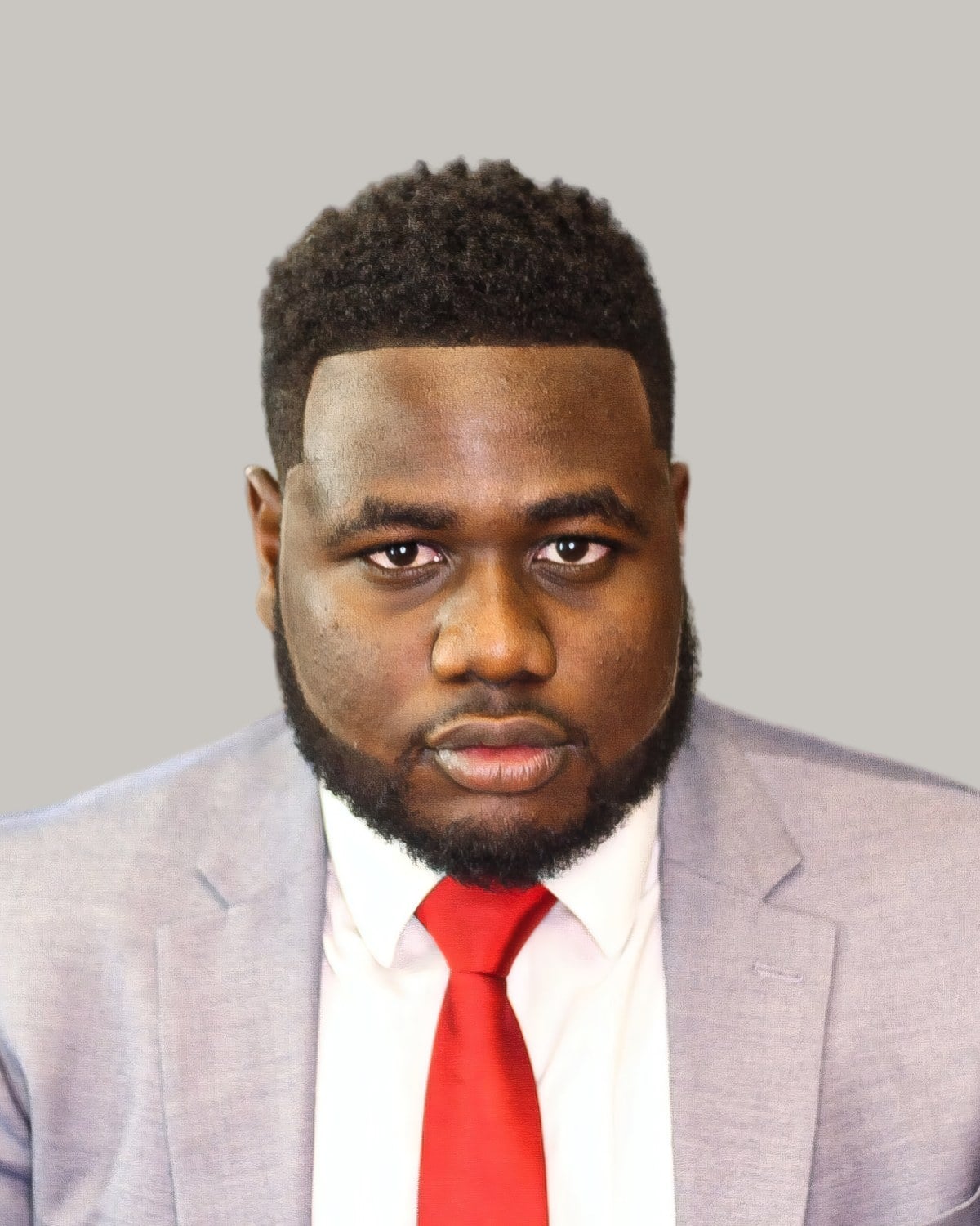 Bearded man with a short afro, a sharp shape-up and a low fade, in a gray suit and red tie
