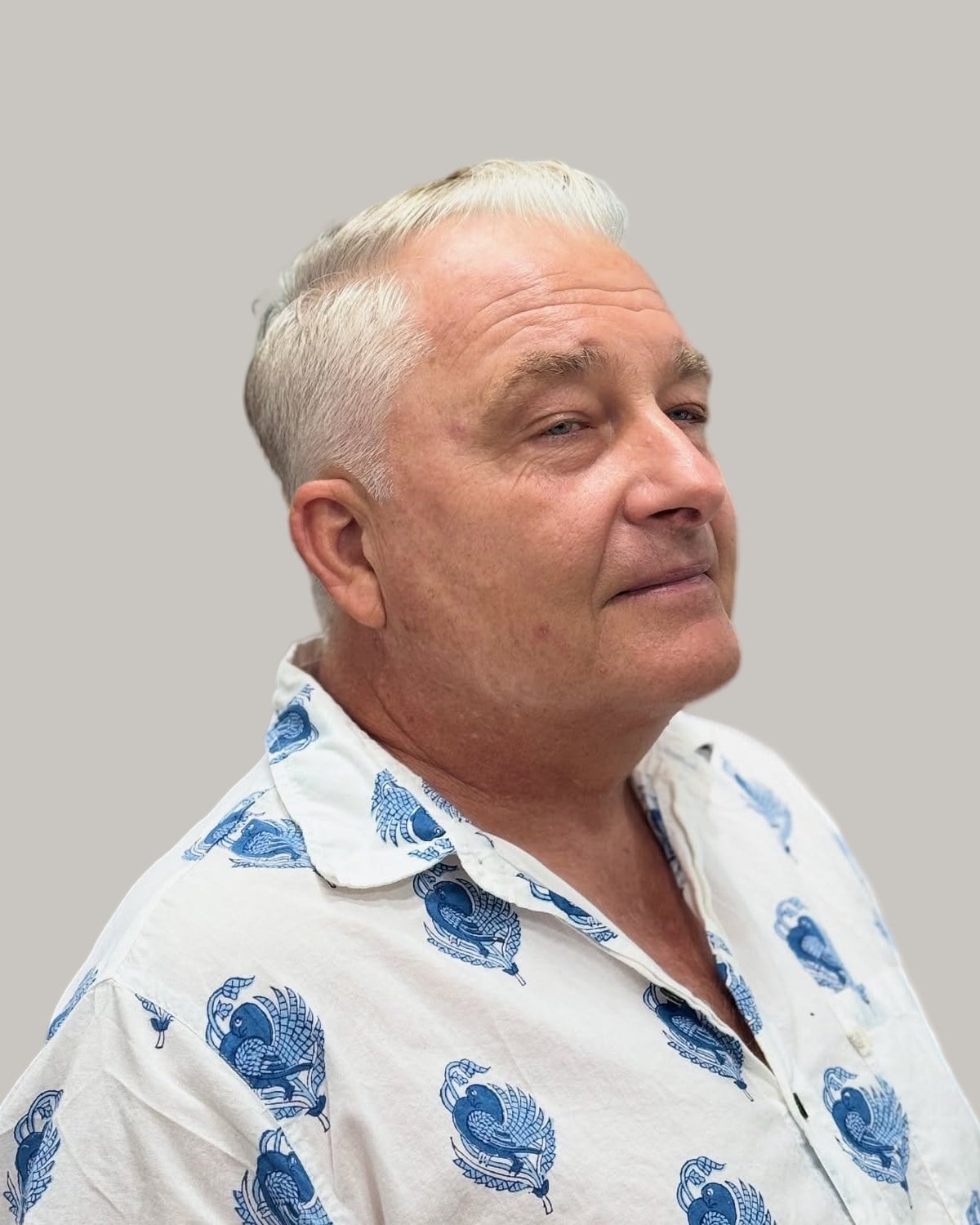 Older man with short silver hair swept over a close-cut side, in a blue-patterned white shirt, seen in three-quarter view