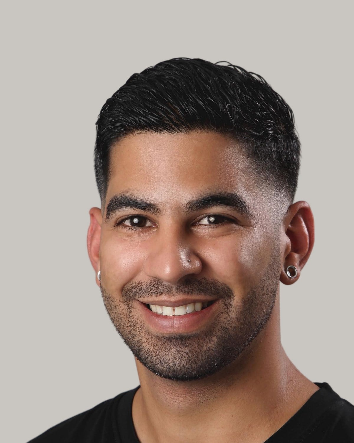 Smiling man with short dark hair combed back over a low fade, and light stubble