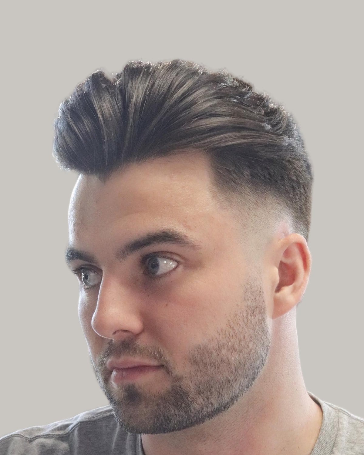 Man with a smooth swept-back quiff, a high skin fade and a short stubble beard, in a gray T-shirt, looking to the side