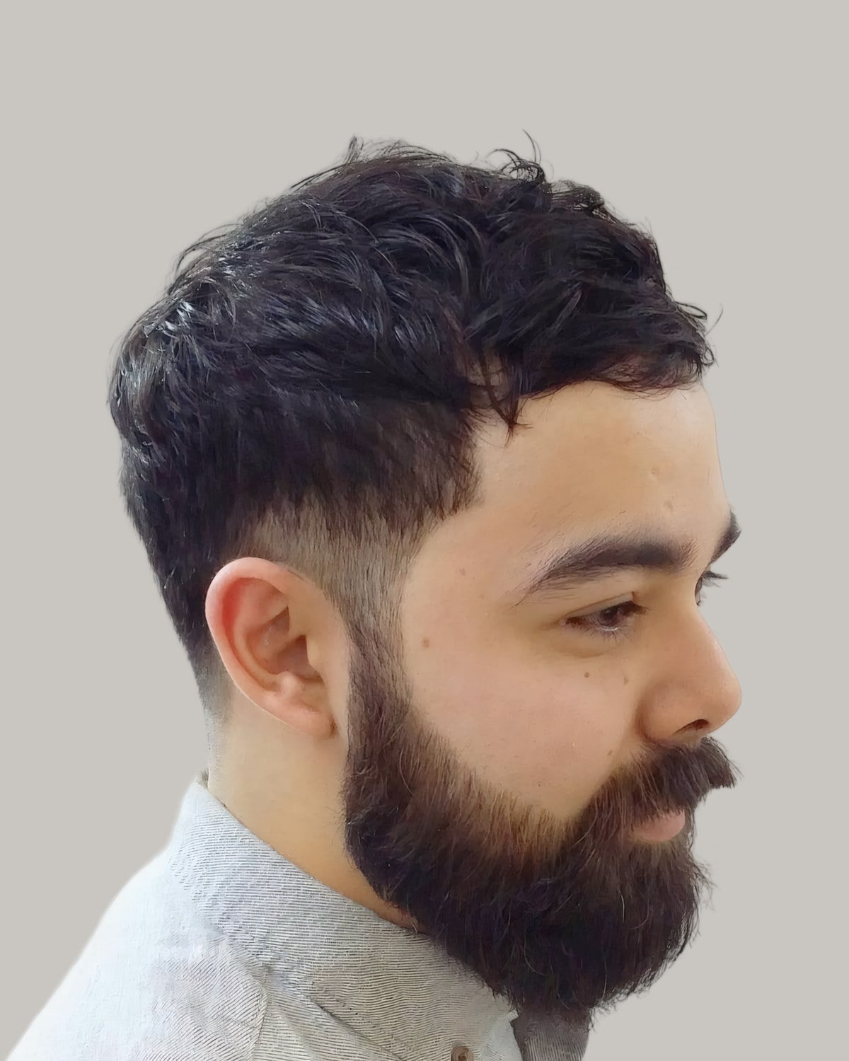 Bearded man with a short, wavy top and a fade at the temple, seen in profile
