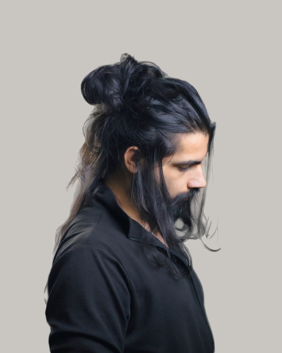 Bearded man with long black hair, the top tied in a knot, seen in profile looking down