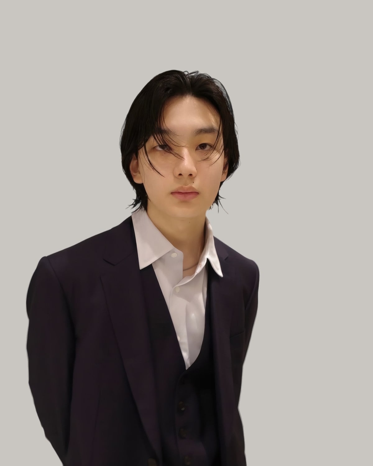 Young man in a dark suit with layered black hair and long bangs parted in the centre