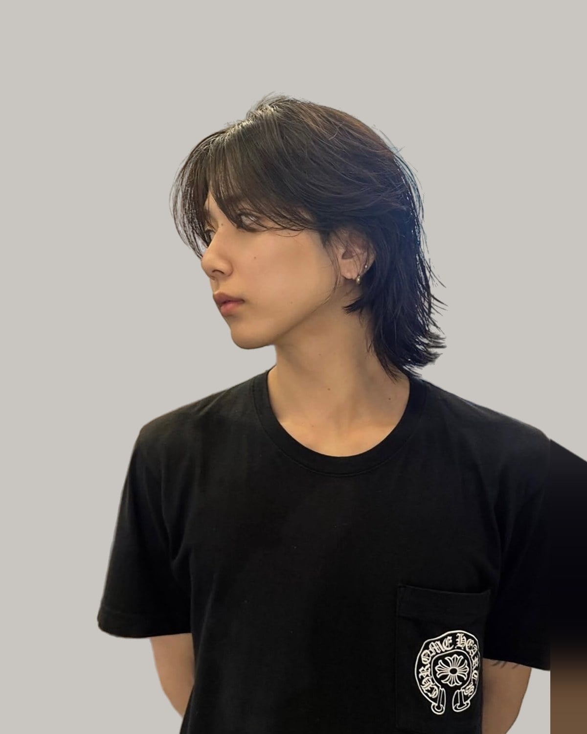 Young man with long, layered black hair falling to his neck, seen in profile